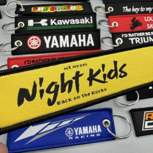 Close-up display of black, yellow and blue embroidered motorcycle key tags with metal eyelets and split rings