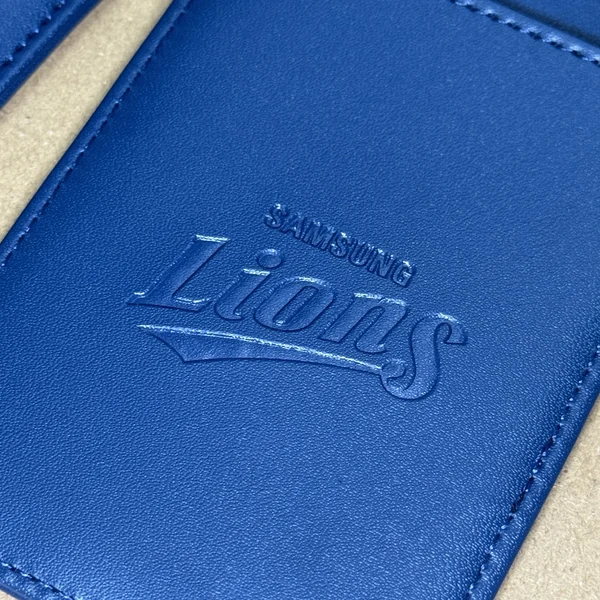 Close-up of a blue leather-style card holder with an embossed Lions logo and stitched edge.