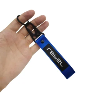 Hand holding a blue short motorcycle wristlet keychain with a black sewn logo patch and split ring