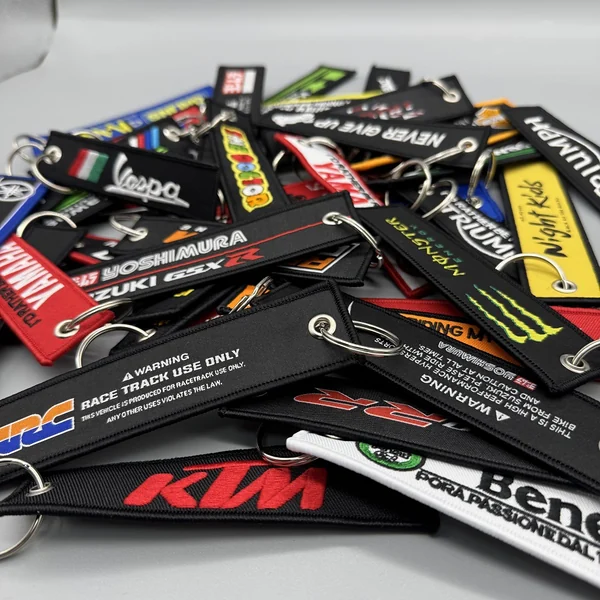 Pile of assorted embroidered motorcycle and automotive fabric key tags with metal split rings