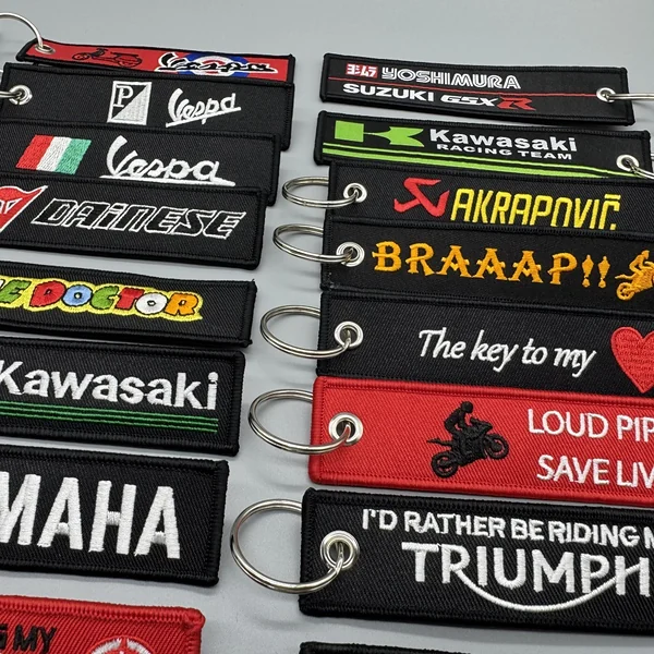 Close-up rows of black, red and green embroidered racing key tags with stitched borders, metal eyelets and split rings