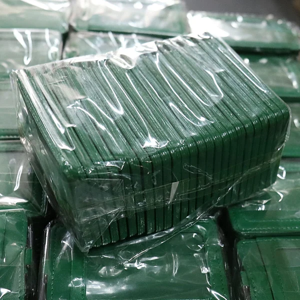 Stack of green ID card holders individually wrapped in clear plastic among packaged stock.