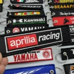 Hand holding a red and black embroidered racing key tag above assorted motorcycle keychains