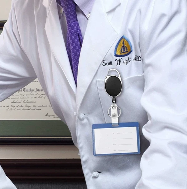 Round badge reel holding a blue ID card holder on the chest of a white coat
