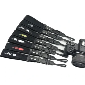 Assorted black camera straps with brand lettering, adjusters and narrow attachment ends beside a camera