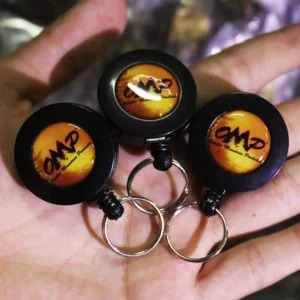 Three black round badge reels with orange logo inserts and metal key rings