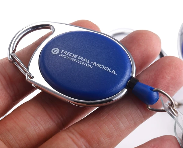 Hand holding a blue oval logo badge reel with integrated carabiner and metal key ring