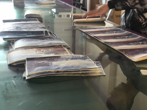 Stacks of printed sheets and panels on a factory worktable with a worker in the background
