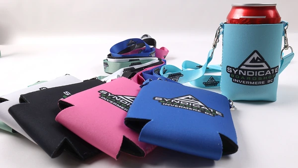 Flat can coolers in assorted colors beside a turquoise cooler holding a red beverage can