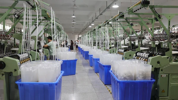 Rows of weaving machines produce webbing in a lanyard factory.