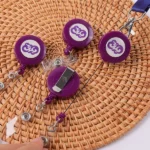 Purple round logo badge reels with clear snap straps and a metal back clip