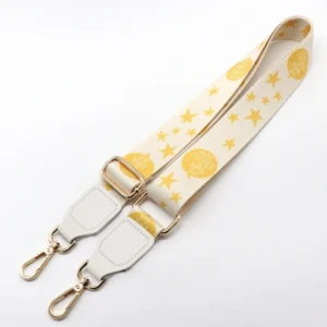 Yellow star-patterned bag strap with white end tabs, adjustment slider and gold-colored swivel clips