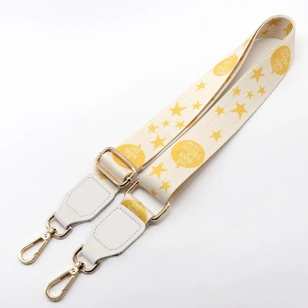 Yellow star-patterned bag strap with white end tabs, adjustment slider and gold-colored swivel clips