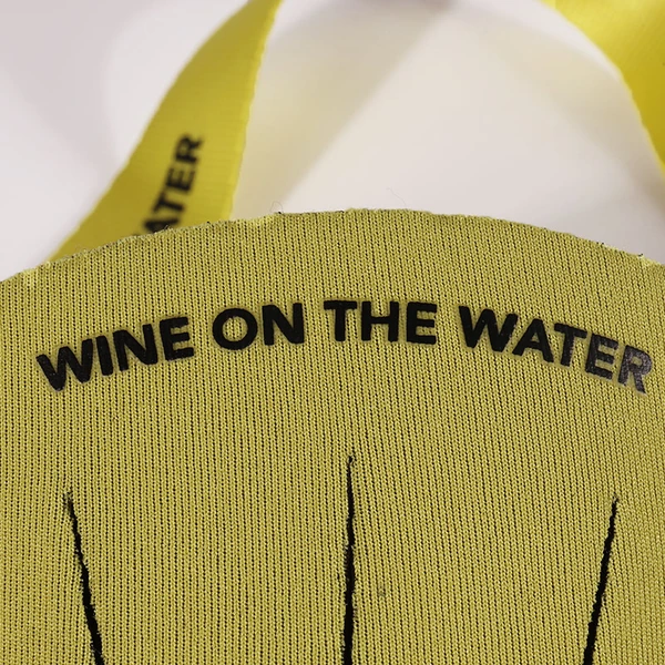 Close-up of black WINE ON THE WATER lettering and printed lines on a yellow wine glass holder